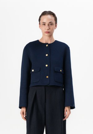 Marinblå ulljacka med rund halsringning, lång ärm, guldfärgad knäppning och två framfickor. Kort design med en texturerad yta.