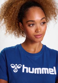 Blå bomulds T-shirt med et stort hvidt "hummel" logo med en bi grafik, rund halsudskæring og korte ærmer. Glat tekstur.