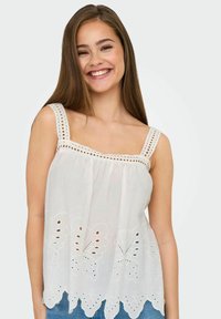 Top bianco senza maniche con scollatura quadrata, ricca di ricami a farfalla e orlo a scallop; presenta dettagli ad occhiello sulle spalline.