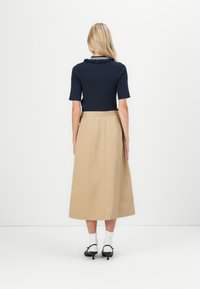 Marineblå ribbestrikket topp med korte ermer, kombinert med en beige midiskjørt. Skjørtet har en definert midje og faller underleggen. Svarte hæler og hvite sokker.