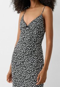 Vestido floral en blanco y negro con tirantes finos, corsé ajustado y falda fluida. Presenta pequeñas flores blancas sobre un fondo oscuro.