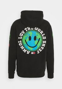 Sudadera negra con capucha que presenta un gran gráfico multicolor de la Tierra y una carita sonriente en la parte posterior, con el texto "AMOR POR EL MUNDO" y detalles de la marca.