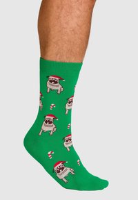 Grüne Socken mit wiederholten Mops-Motiven, die rote Weihnachtsmützen und Zuckerstangen tragen, aus weichem Material mit enger Passform.