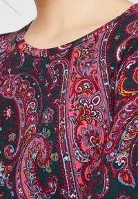 Dark fabric features a red and blue paisley pattern, with intricate swirls and floral details. The neckline is rounded.