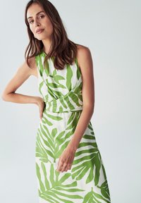 Hihaton mekko valkoisesta kankaasta, jossa on vihreä lehtikuvio, vyötäröltä kireä ja täyspitkä hame. Sujuva pinta ja luonnollinen muotoilu.