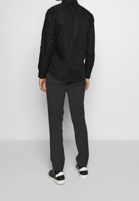 Maglietta nera a maniche lunghe con chiusura a bottoni, abbinata a pantaloni grigi. Sneakers con una combinazione di colori bianco e nero. Tessuto dalla textura liscia.