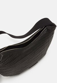 Borsa in pelle intrecciata nera con forma curva, dotata di una robusta fettuccia in tessuto e dettagli in zip color oro per la chiusura.