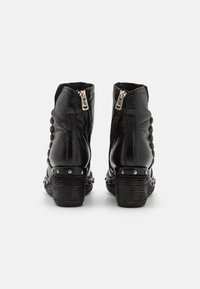 Botas de cuero negro hasta el tobillo con un tacón texturizado, cierres de cremallera y acentos de tachuelas en los laterales. Punta redonda y detalle de paneles distintivos.