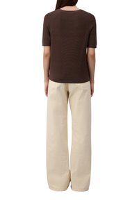 Pull marron à manches courtes avec une texture côtelée, associé à un pantalon ample de couleur crème avec des poches arrière.