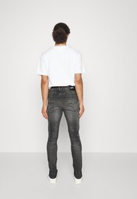 Vaqueros de mezclilla grises con un corte ajustado, que presentan bolsillos traseros y una etiqueta negra en la cintura. Combinados con una camiseta blanca sencilla.