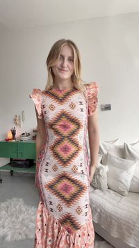 Vestido estampado com mangas com babados, apresentando designs geométricos em rosa, castanho e turquesa sobre um fundo claro. Parte inferior evasê.