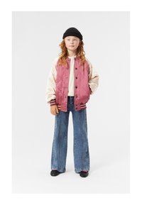 Giacca bomber trapuntata rosa e crema, maniche lunghe, berretto in maglia nero, camicia bianca, jeans blu in denim a zampa d'elefante, scarpe nere.