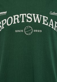 Zielona koszulka z białym napisem "SPORTSWEAR" i grafiką siatkówki, wykonana z miękkiego, gładkiego materiału.