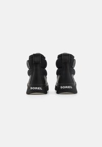 Svarta hög-top sneakers med ett vadderat ovandel, texturerad gummisula och framträdande vit varumärkeslogotyp på baksidan. Slät och vadderad design.