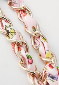 Růžový řetěz z látky s květinovým vzorem a kovovými články v zlatém tónu, který má pletený design a hladkou texturu. Výrazné barevné květinové akcenty.