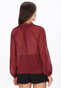 Punaharmaa pitkähihainen pusero, valmistettu läpikuultavasta kankaasta, jossa on rypytetty pääntie ja leveät hihat, pehmeä tekstuuri ja virtaava muotoilu.