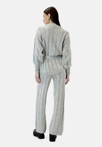 Jersey de punto gris claro y pantalones de pierna ancha con textura acanalada, cintura con cinturón y mangas largas, usados con zapatos negros de plataforma.