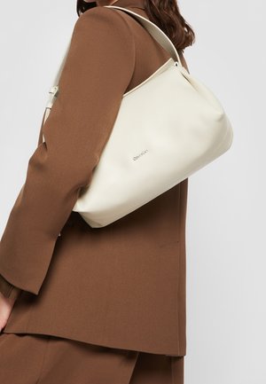 Sac à épaule en cuir blanc avec une texture lisse, une forme arrondie et un logo subtil à l'avant. Bandoulière réglable pour un transport facile.