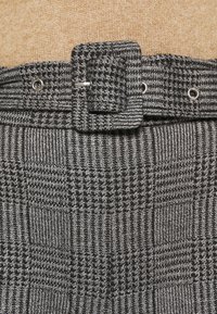 Grå och svart rutig tyg med en texturerad yta. Har en fyrkantig spänne och metallöglor för justerbar fastsättning.