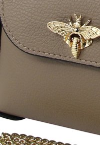 Beige leren handtas met een textuurafwerking, voorzien van een gouden bij-embleem op de klep en een decoratieve gouden kettingriem.