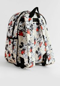 Un sac à dos avec un fond crème présentant un motif répété de Mickey Mouse en noir et rouge. Des bretelles et des zippers noirs complètent le design.