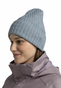Light blue ribbed knit beanie with a pointed top. Worn with a high-collared purple jacket. Soft texture, fitted design.