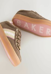Hnědé semišové tenisky se zlatým a růžovým pruhovaným detailem po straně a zlatými oky. Průhledná růžová podešev nese nápis "BAKER" bílým písmem.