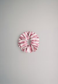 Roze-wit gestreepte stoffen scrunchie liggend plat op een neutrale lichtgrijze achtergrond.