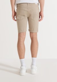 Beige korte broek van katoen, met opgerolde mouwen, twee achterzakken en een slim fit. Draagt bij witte sneakers en crew sokken.
