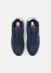 Sneakers blu navy con rete testurizzata e pelle liscia. Presentano dettagli bianchi e una striscia rossa. Lacci e linguetta imbottita con il marchio visibile.