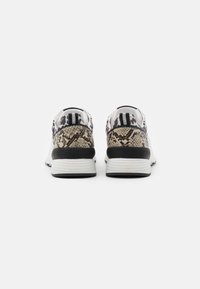 Ein Paar Sneakers, von hinten gezeigt, mit gemischten Tierdruckmustern, schwarzen und weißen Absätzen sowie weißen Sohlen auf einem schlichten Hintergrund.