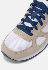 Sneaker in suede beige con pannelli in rete bianca, lacci blu navy e cuciture a contrasto. Presenta una punta arrotondata e suola imbottita.