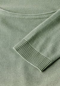 Grüner gestrickter Pullover mit rundem Halsausschnitt, ausgestattet mit gerippten Bündchen. Die Textur ist glatt mit einem feinen Strickmuster.