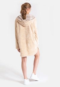 Beżowy puszysty hoodie z wyściełanym wierzchołkiem w kratę, o luźnym kroju i bocznych rozcięciach. W połączeniu z białymi butami sportowymi.