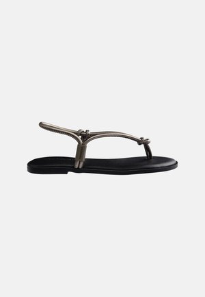 Sandale plate noire avec des fines lanières métalliques et une petite étiquette de marque sur le côté, conçue pour un port estival décontracté.