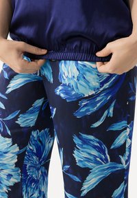 Pantaloni floreali blu navy con grandi motivi di fiori bianchi e blu. La parte superiore è di un blu navy uniforme con una vita elastica arricciata.