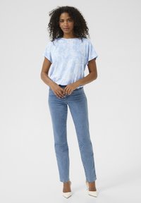 Light blue short-sleeve top with white paisley pattern, paired with light blue fitted jeans and beige high-heeled shoes.