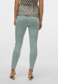 Mintgrüne Leggings mit glatter Textur, figurbetontem Design und Knöchellänge, kombiniert mit einem gemusterten Oberteil. Sichtbares, einfaches, modernes Schuhwerk.