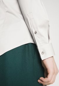 Camisa de manga larga gris claro con puños de botón, combinada con una falda verde texturizada. La camisa tiene una tela suave y costuras precisas.