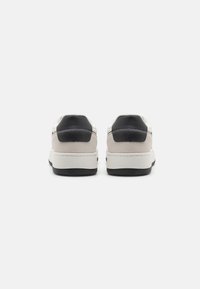 Sneakers featuring a combination of white leather and gray suede, with black accents on the heel, a sturdy white midsole, and a textured black outsole.