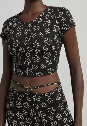 Czarny kwiatowy crop top z krótkimi rękawami, okrągłym dekoltem i dopasowanym fasonem, ozdobiony białymi haftowanymi kwiatami. Zawiera detal w postaci wycięcia z akcentem w formie pierścionka.
