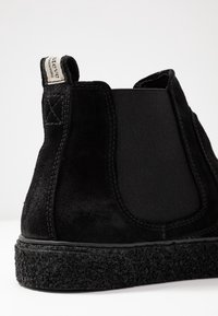 Stivale alla caviglia in camoscio nero con pannelli elastici laterali, suola testurizzata e linguetta ad anello con etichetta. I dettagli cuciti accentuano il design.