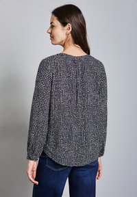 Långärmad blus i marinblått med ett geometriskt vitt mönster. Har veck bak och en rund halsringning. Mjukt, lätt tyg.