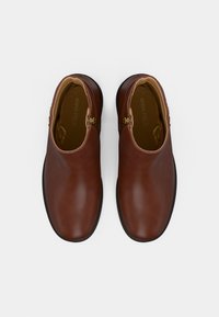 Cizme de gleznă din piele maro cu un finisaj neted, prezentând două fermoare laterale, vârf rotund și talpă din cauciuc negru. În interior, etichetat "ANNA FIELD."