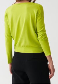 Maglione a maglia verde lime con maniche lunghe, una vestibilità morbida e dettagli a coste sull'orlo, abbinato a pantaloni neri su misura.