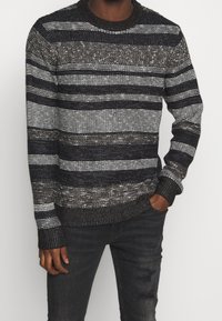 Handstickad tröja i svart och vitt med horisontella ränder. Har ribbade ärmslut och halsringning, med ett texturerat garn och en avslappnad passform.