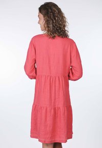 Pfirsichfarbenes Leinenkleid mit langen Ärmeln, gestuftem Design und dekorativem Spitzenbesatz am Saum. Glatte Textur und lockere Passform.