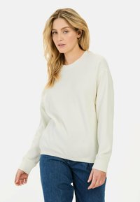 Crème-kleurige gebreide sweatshirt met een ontspannen pasvorm, ronde halslijn en lange mouwen. Gecombineerd met donkerblauwe denim jeans.
