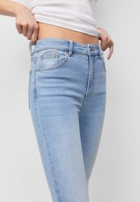 Jean en denim bleu clair avec design à cinq poches, surpiqûres contrastantes, taille mi-haute et silhouette slim.