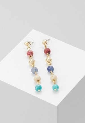 Boucles d'oreilles couleur or avec perles multicolores : rouge, bleu, crème et turquoise, suspendues à une chaîne en or, avec des attaches transparentes.